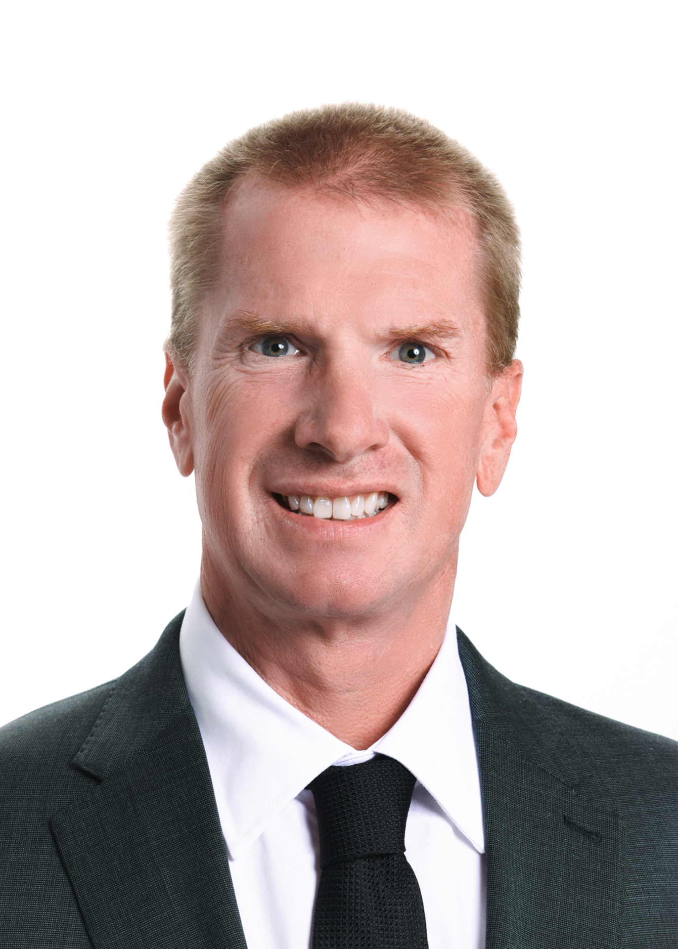 Head-and-shoulders portrait of a smiling man in a dark suit and black tie against a white background, looking at the camera.